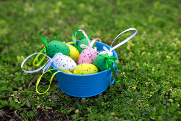 Decorative multi-colored Easter eggs with ribbons lie in a blue box on a green grass background