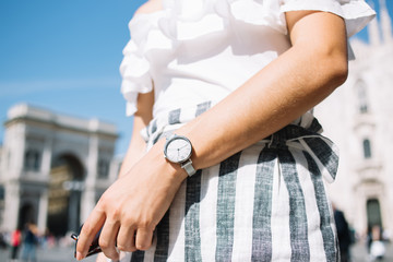 Cropped image of woman in trendy clothes and wristwatch in metalic silver colour with minimalistic screen, expensive timepiece with quality accuracy design and chrome display on woman's hand outdoors