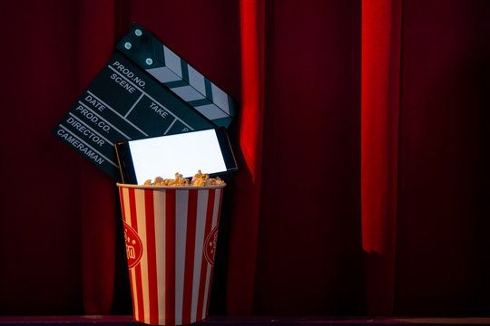 Mobile Phone With Empty White Bright Screen With Popcorn Bucket And Movie Clapper Board. Concept Of Streaming TV On Internet Phone.