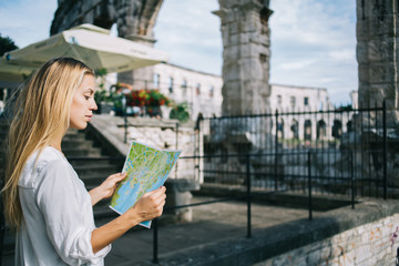 Pensive blonde female traveler concentrated on searching routes explore historical monuments and landmarks in city, thoughtful woman 20s holding map during sightseeing tour on vacation holidays