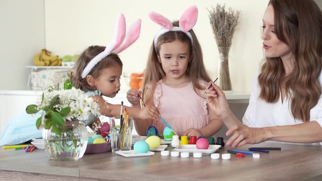 happy family preparing for easter. mother with daughters with funny bunny ears painting easter eggs together