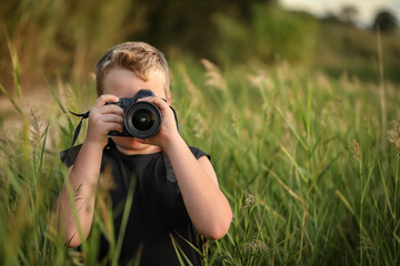 Young boy hiding in long grass near a lake taking photos with a dslr full frame camera