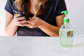 hygiene against viruses and bacteria, woman using smartphone in front of desk with hand sanitizer on it