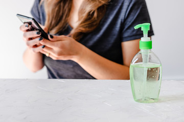 hygiene against viruses and bacteria, woman using smartphone in front of desk with hand sanitizer on it
