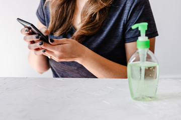 hygiene against viruses and bacteria, woman using smartphone in front of desk with hand sanitizer on it