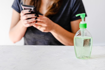 hygiene against viruses and bacteria, woman using smartphone in front of desk with hand sanitizer on it
