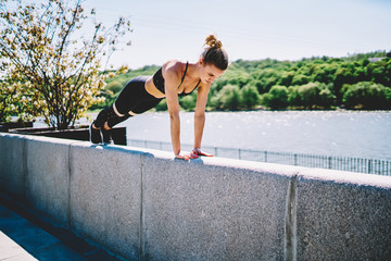 Strong athletic woman standing in plank on concrete fence