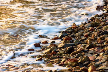 Small stones on the shore with the foam of the waves during tropical sunset