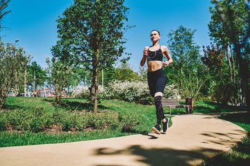 Strong jogger in earphones running with smartphone on alley in park in bright day