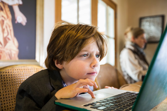 A six year old boy typing on a laptop at home, using the cursor touch pad.