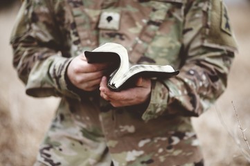 Shallow focus shot of a young soldier  holding an open bible in a field