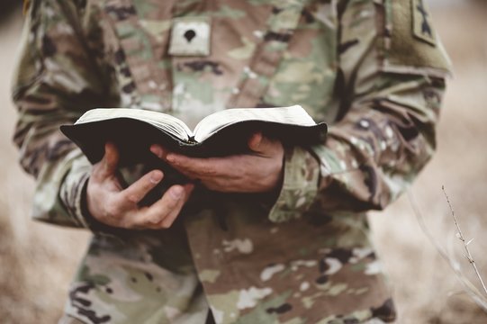 Shallow focus shot of a young soldier holding an open bible in a field