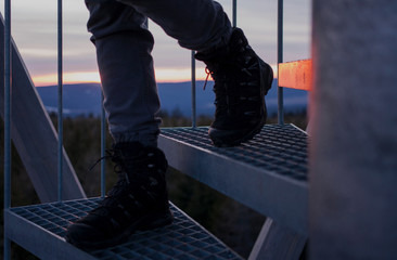 Legs walking down metal contruction side stairs at mountain tower sunset sky light