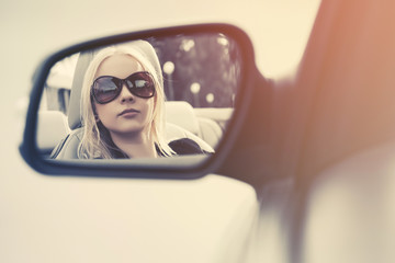Blonde fashion woman in sunglasses looking in the car rear view mirror
