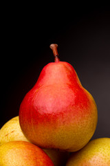 Still life of vibrant colourful yellow red Seckel pear resting on other pears contrasted against a dark studio background
