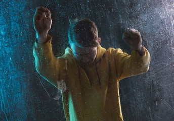 A young guy in a yellow hoodie is sad behind a blind window