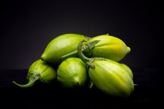 Still life studio shot of a lot of vibrant green scarlet eggplant vegetables against a black background. Graphic minimalist image of food.