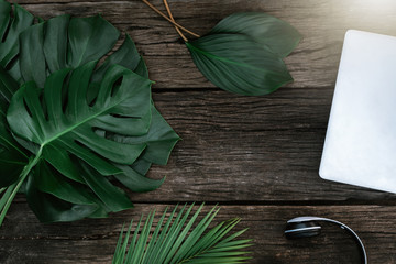 Flat lay creative frame of tropical nature leaves Monstera on rustic wood grunge background with retro computer and Headphones, tropical jungle vacation and travel concepts. 