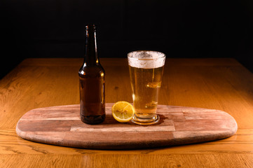 Isolated fresh beer on wooden table with bottle and lemon,black background