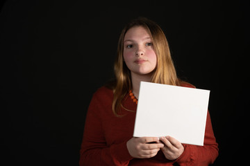Teen girl holding a small white sign on a black background with room for your copy.