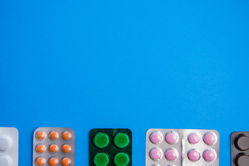 Frame of pills in white foil blisters capsule tablet packaging lay flat in a row on the bottom isolated on blue background. For pharmaceutical, medical and science theme.