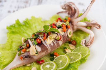 Spicy lemon squid with galangal, chilies, carrots, peppermint, spring onions and garlic on a plate on a white wooden floor.