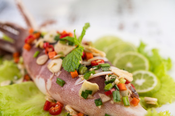 Spicy lemon squid with galangal, chilies, carrots, peppermint, spring onions and garlic on a plate on a white wooden floor.