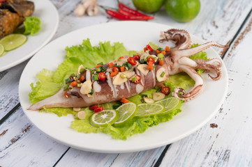 Spicy lemon squid with galangal, chilies, carrots, peppermint, spring onions and garlic on a plate on a white wooden floor.