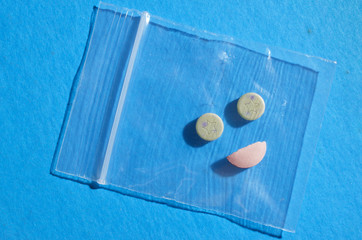 Drug dependence, illustrated by pills arranged to look like happy face, implying depending on drug or substance to feel well. Blue background represents "feeling blue".