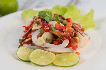 Spicy lemon squid with galangal, chilies, carrots, peppermint, spring onions and garlic on a plate on a white wooden floor.