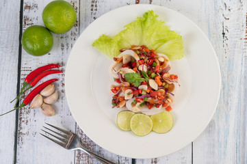 Spicy lemon squid with galangal, chilies, carrots, peppermint, spring onions and garlic on a plate on a white wooden floor.