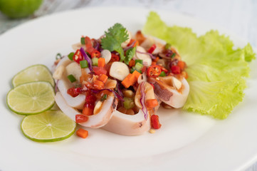 Spicy lemon squid with galangal, chilies, carrots, peppermint, spring onions and garlic on a plate on a white wooden floor.