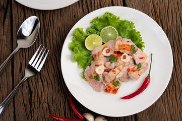 Spicy lime pork with salad, galangal, chilli, tomato and garlic on a white plate on a wooden floor.