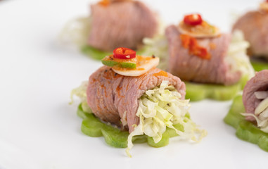 Spicy lime pork salad with bitter melon, galangal, chili, tomatoes and garlic in a white plate on a black cement floor.