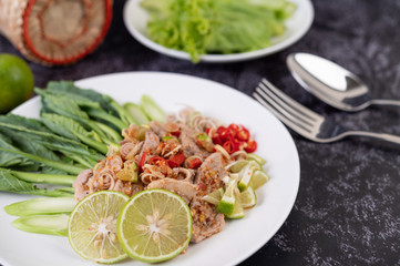 Spicy lime pork salad with kale, galangal, chilli and garlic in a white plate on a black cement floor.