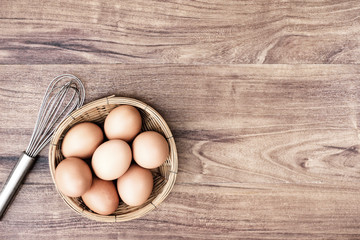 Top view of raw eggs in the basket and Straw or chaff  with Egg beater on wooden table.vintage filter.