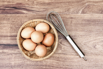 Top view of raw eggs in the basket and Straw or chaff with Egg beater on wooden table.vintage filter.