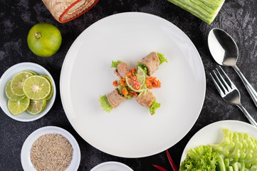 Spicy lime pork salad with bitter melon, galangal, chili, tomatoes and garlic in a white plate on a black cement floor.