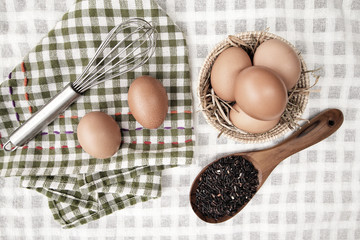 Top view of raw eggs in the basket and Straw or chaff  with Egg beater , hand towel and rice berry in the wooden spoon on white table cloth.