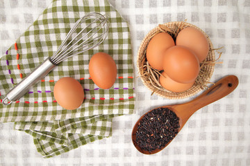Top view of raw eggs in the basket and Straw or chaff  with Egg beater , hand towel and rice berry in the wooden spoon on white table cloth.