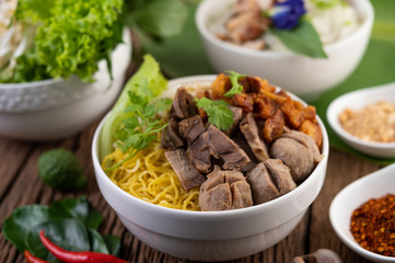 Yellow noodles in a cup with crispy pork, slices of pork, and meatballs together with Thai food-style noodles