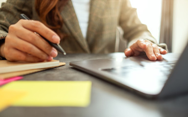 Businesswoman writing on paperwork while typing on laptop computer on the table in office