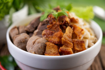Yellow noodles in a cup with crispy pork, slices of pork, and meatballs together with Thai food-style noodles