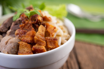 Yellow noodles in a cup with crispy pork, slices of pork, and meatballs together with Thai food-style noodles