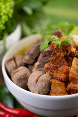 Yellow noodles in a cup with crispy pork, slices of pork, and meatballs together with Thai food-style noodles