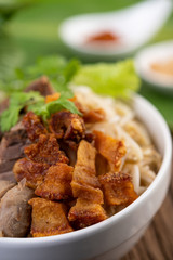 Yellow noodles in a cup with crispy pork, slices of pork, and meatballs together with Thai food-style noodles
