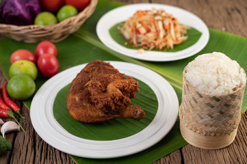 Chicken thighs fried on banana leaves on a white plate with sticky rice.