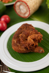 Chicken thighs fried on banana leaves on a white plate
