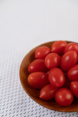Tomatoes placed in a wooden cup on a white cloth.