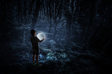 Boy holding moon at night in the forrest